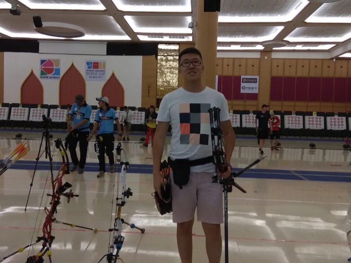 Standing on the competition floor at the Bangkok Indoor Archery World Cup, bows lined up behind.