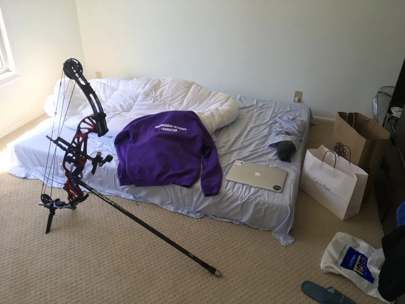 A compound bow leaning against a bed in a San Francisco apartment, moving boxes nearby.
